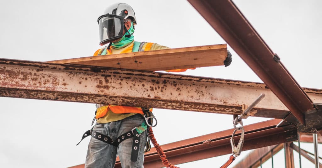Construction worker in face shield stands on a beam holding a 2 by 4 | Workers Compensation Case
