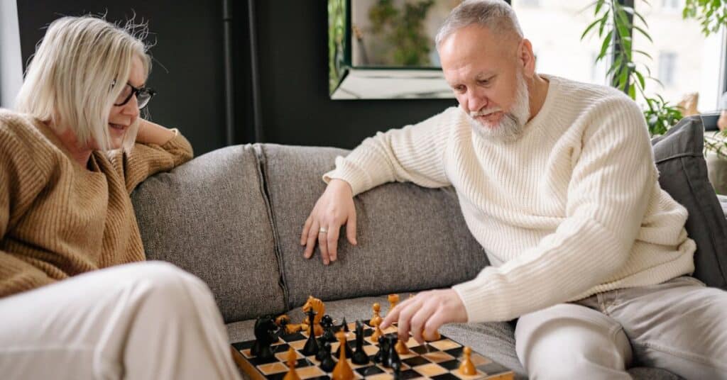 An older couple plays a game of chess while relaxing on the couch