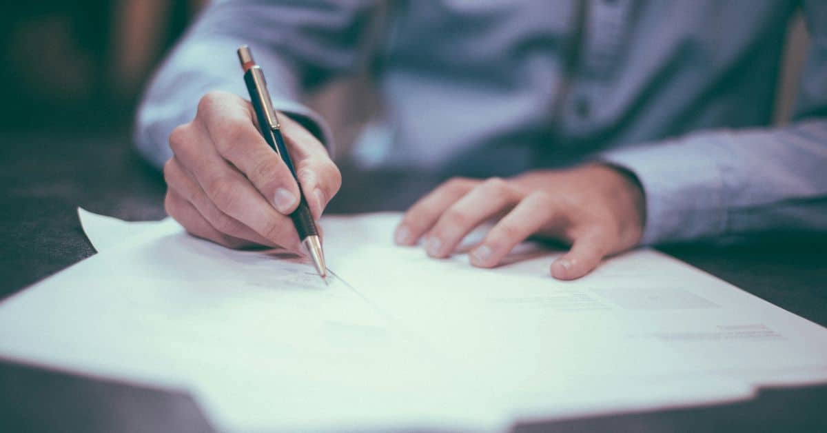 Man holding a pen writing on a stack of papers, Workers' Comp Hearing