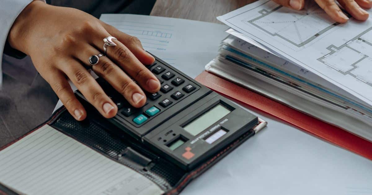 A woman's hand decorated in silver rings rests on a calculator as she works through documents