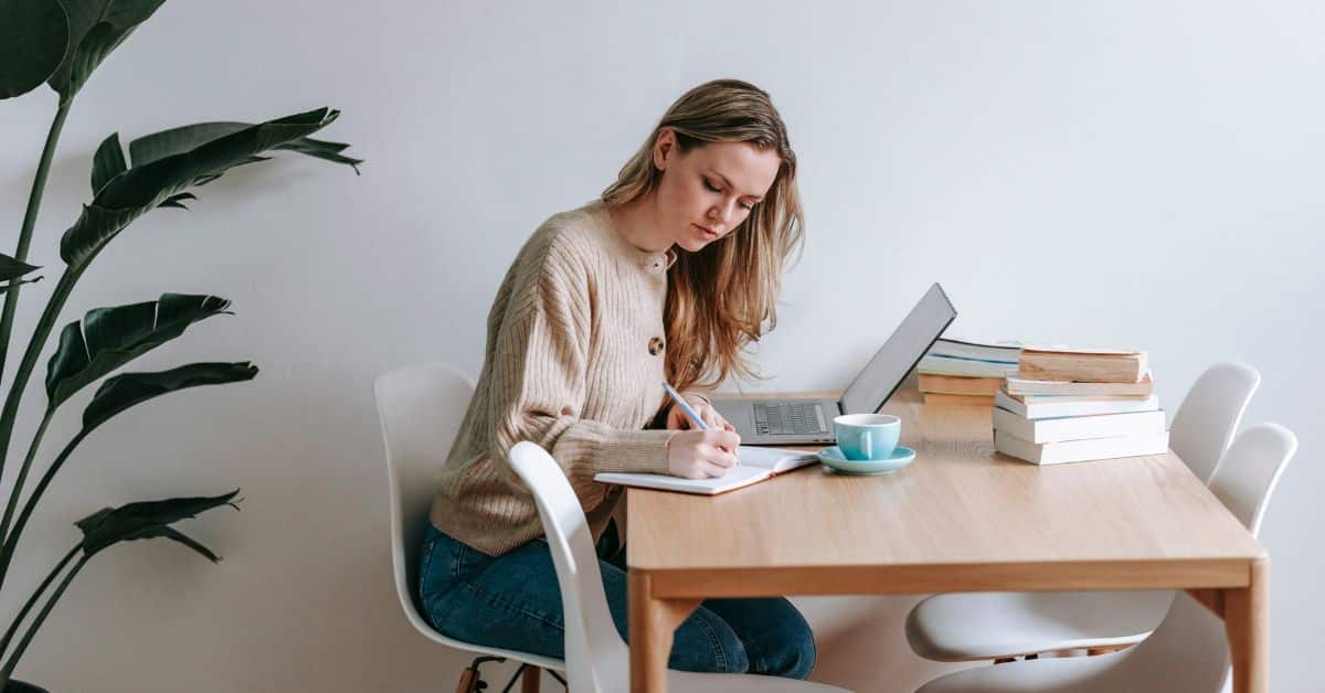 Woman sitting at a table with a notebook and laptop