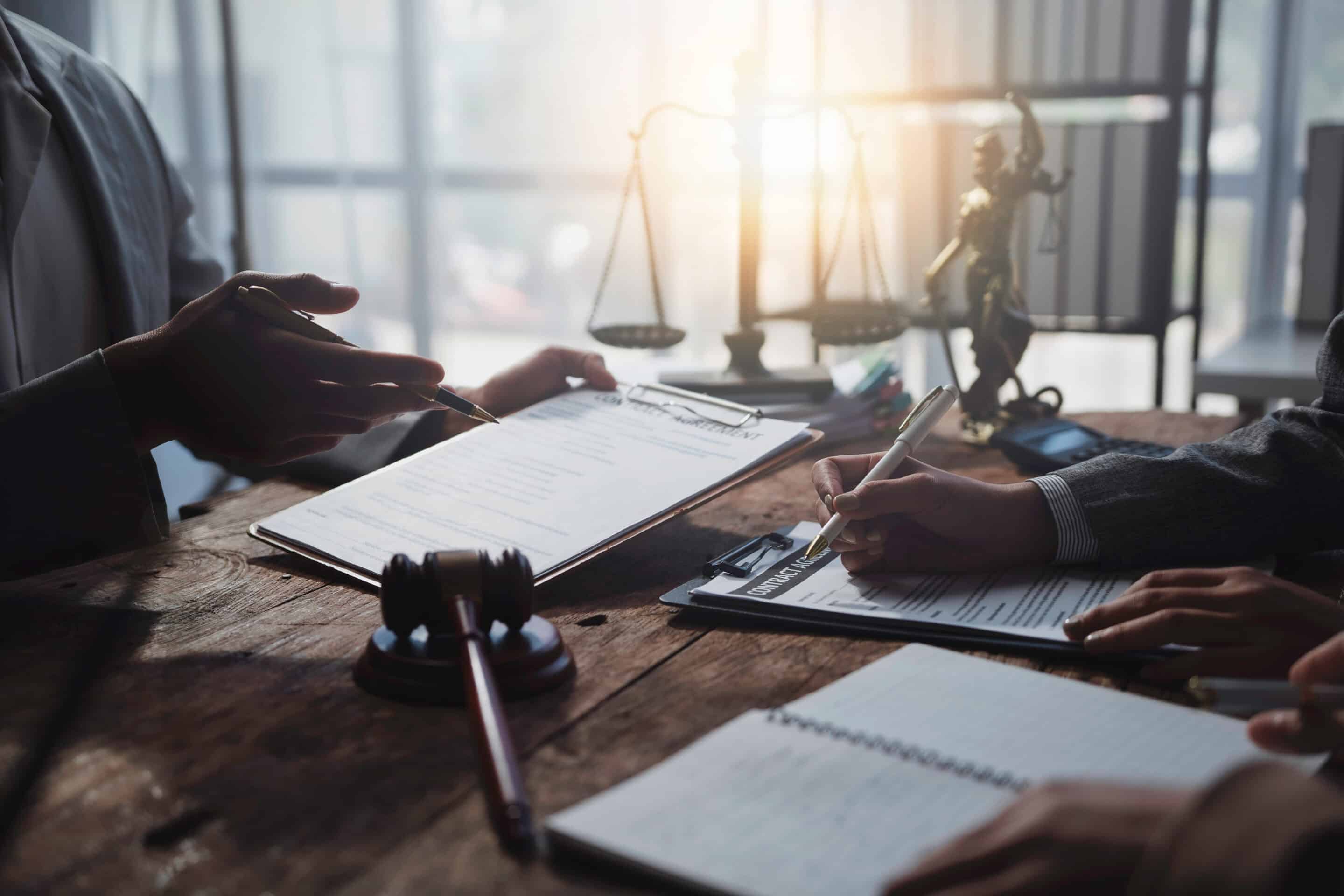 Lawyers working together on a legal document, reviewing and signing agreements in a courtroom setting, with a gavel and scales of justice in the background